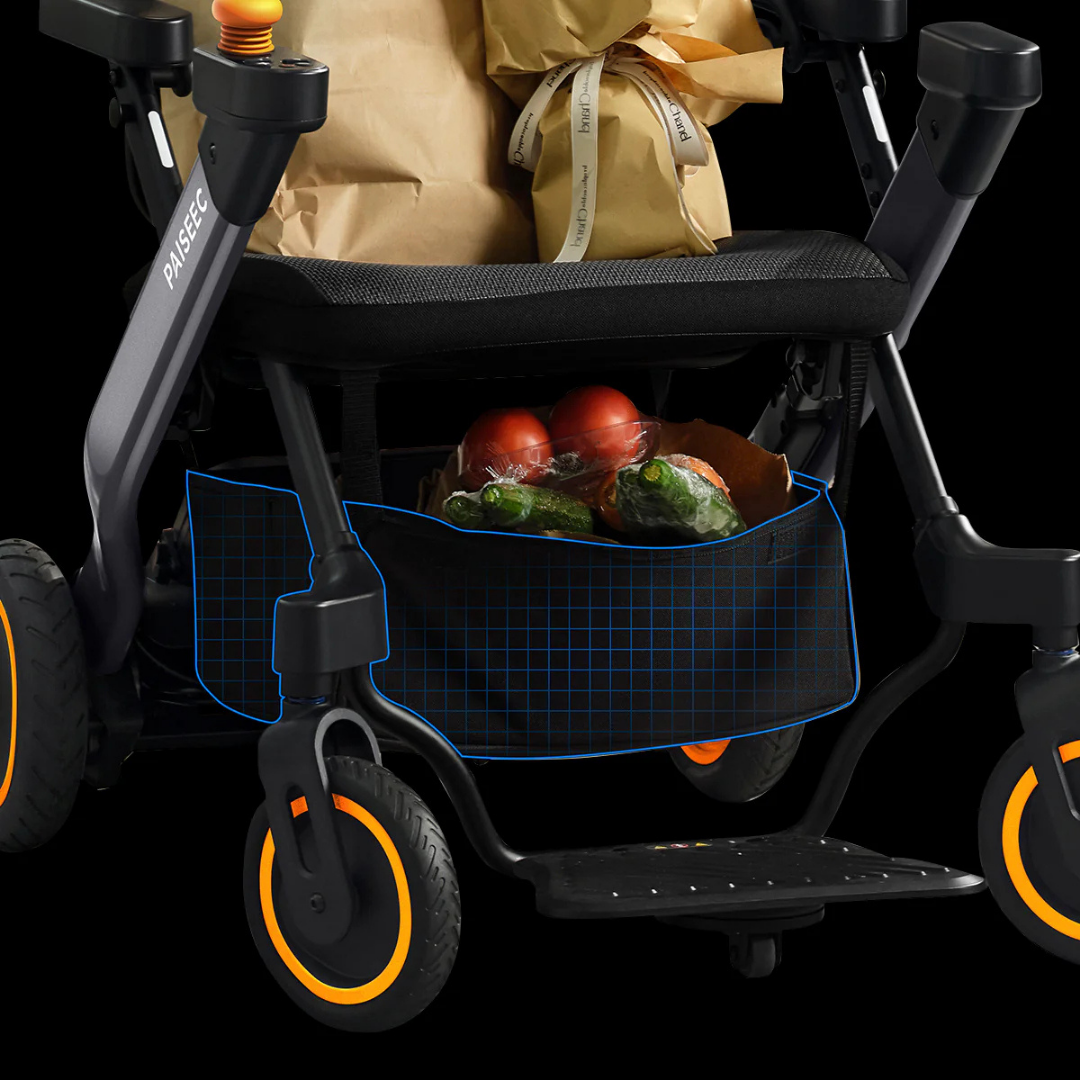 A close-up of Paiseec Electric Wheelchair Parts & Accessories storage pocket holding groceries, including tomatoes and green vegetables in a paper bag. The electric wheelchair features black and orange wheels and folded paper bags on the seat.